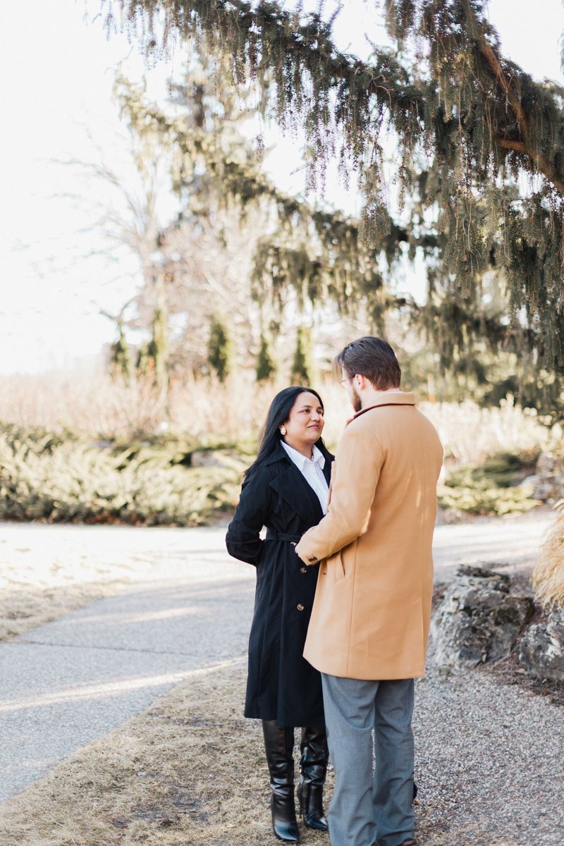 A couple in winter coats share a tender moment on a path beneath hanging moss.