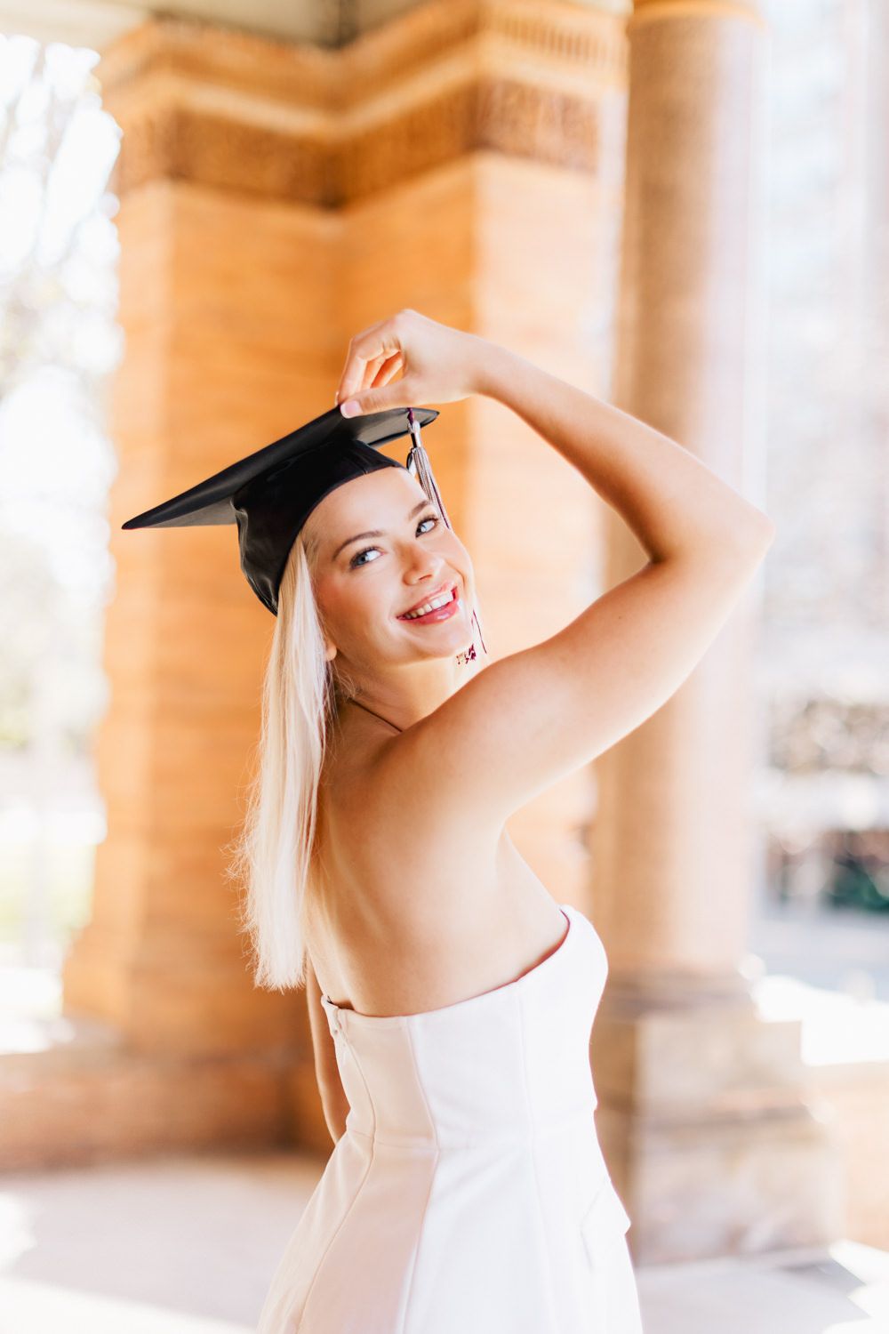 Joyful graduation portrait captured against architectural columns in natural light.