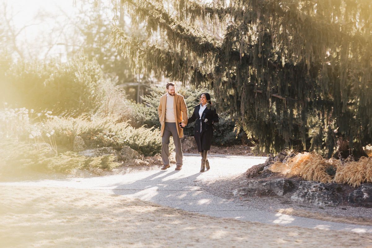 Couple walking together on sunlit path beneath moss-covered trees.