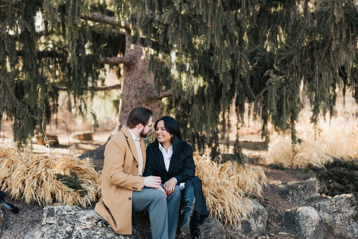 A couple sits closely together on rocks under hanging moss during a romantic outdoor photoshoot.