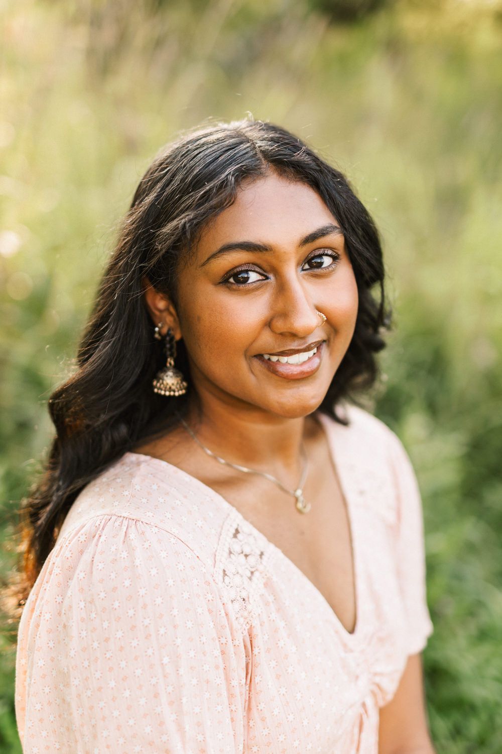 Portrait of a person wearing a peach-colored dress with delicate jewelry against a natural background.