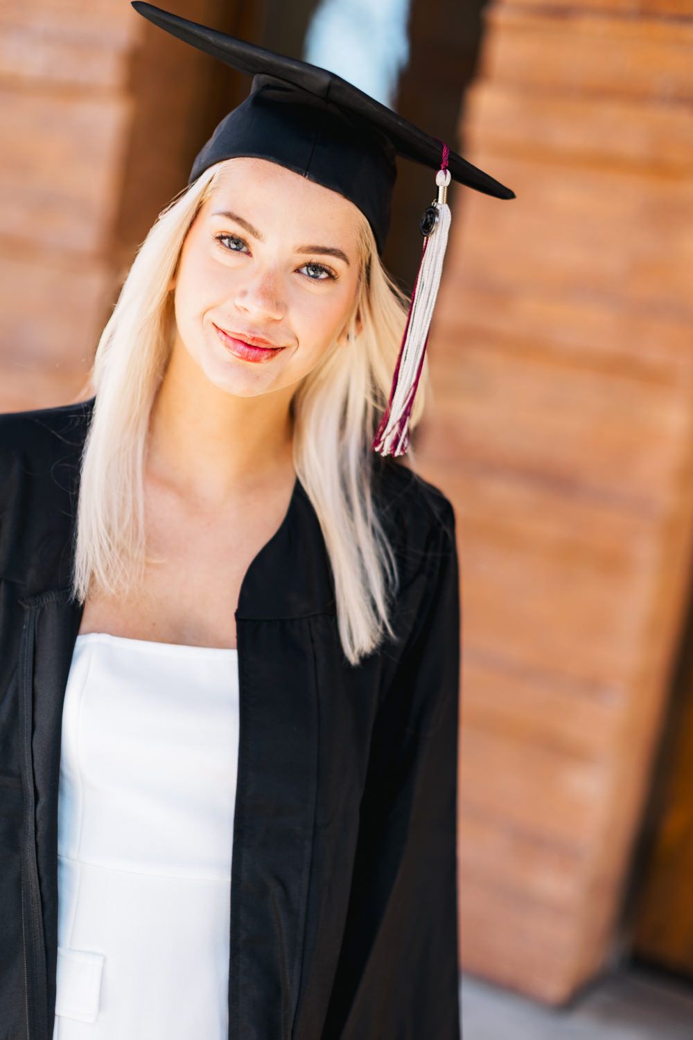 Graduate in academic regalia poses for portrait against warm brick background.