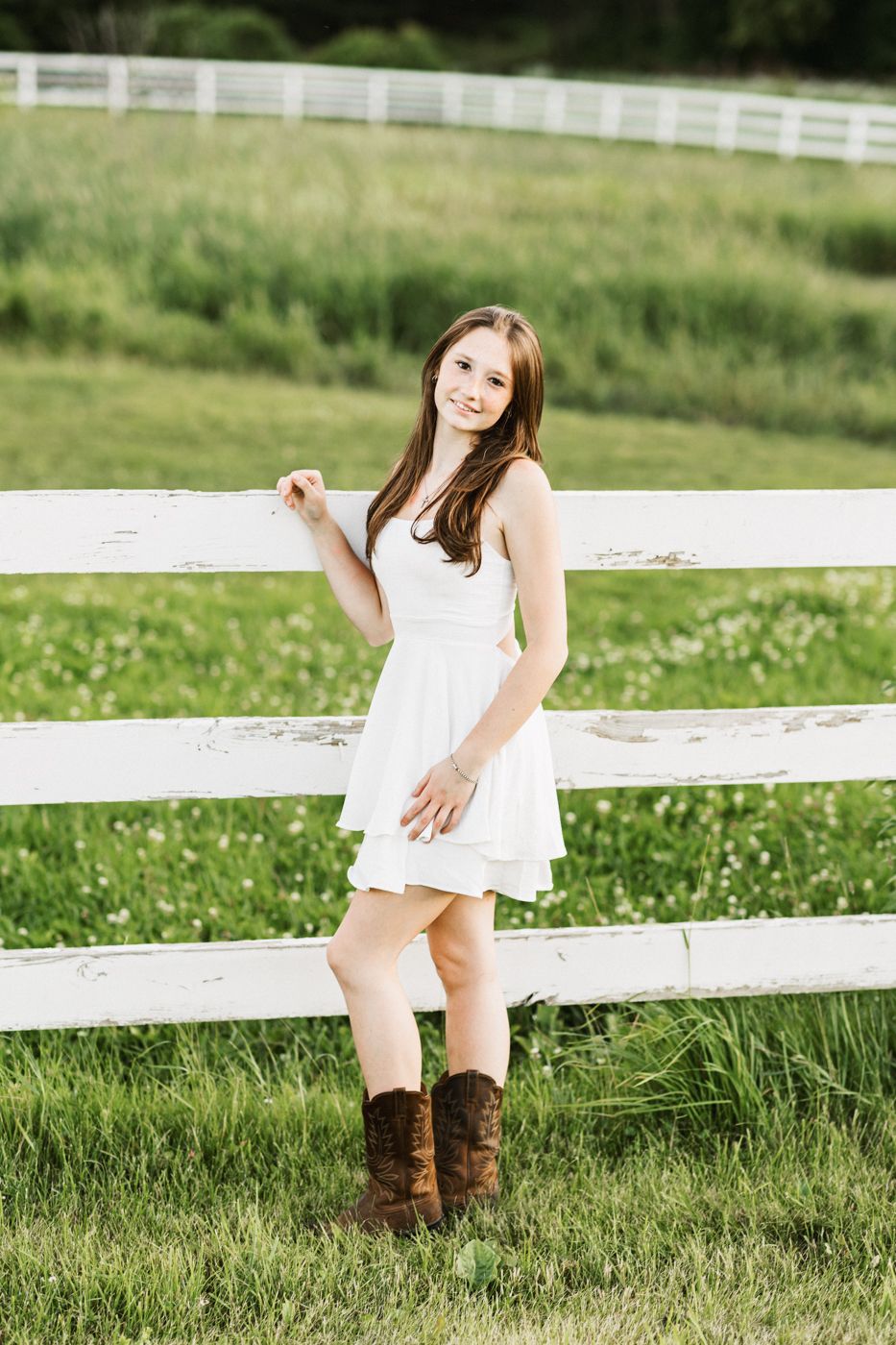 A rustic outdoor scene with white fencing and green pastures in the background.