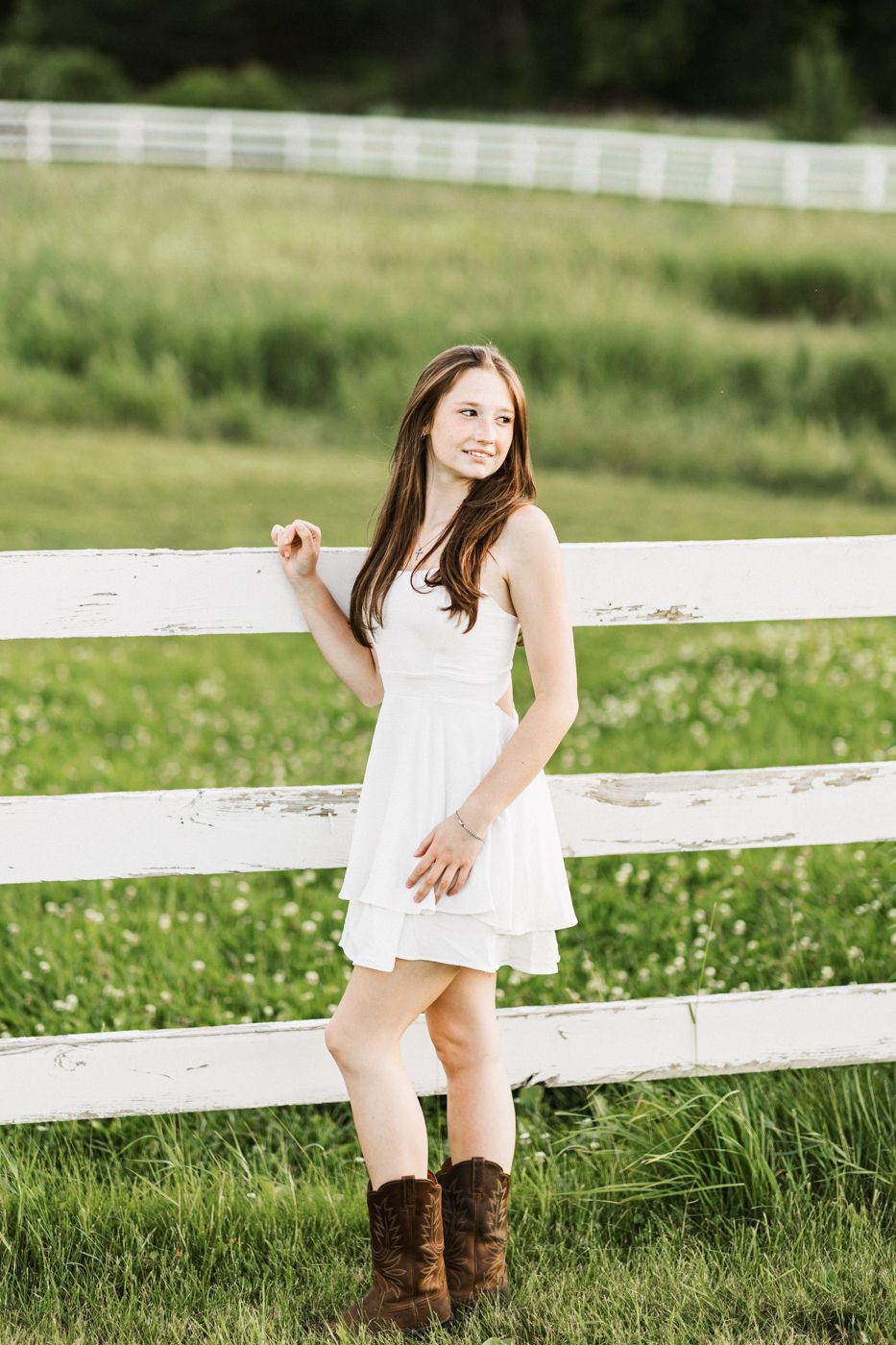 A country-style portrait by a white fence wearing a sundress and brown boots.