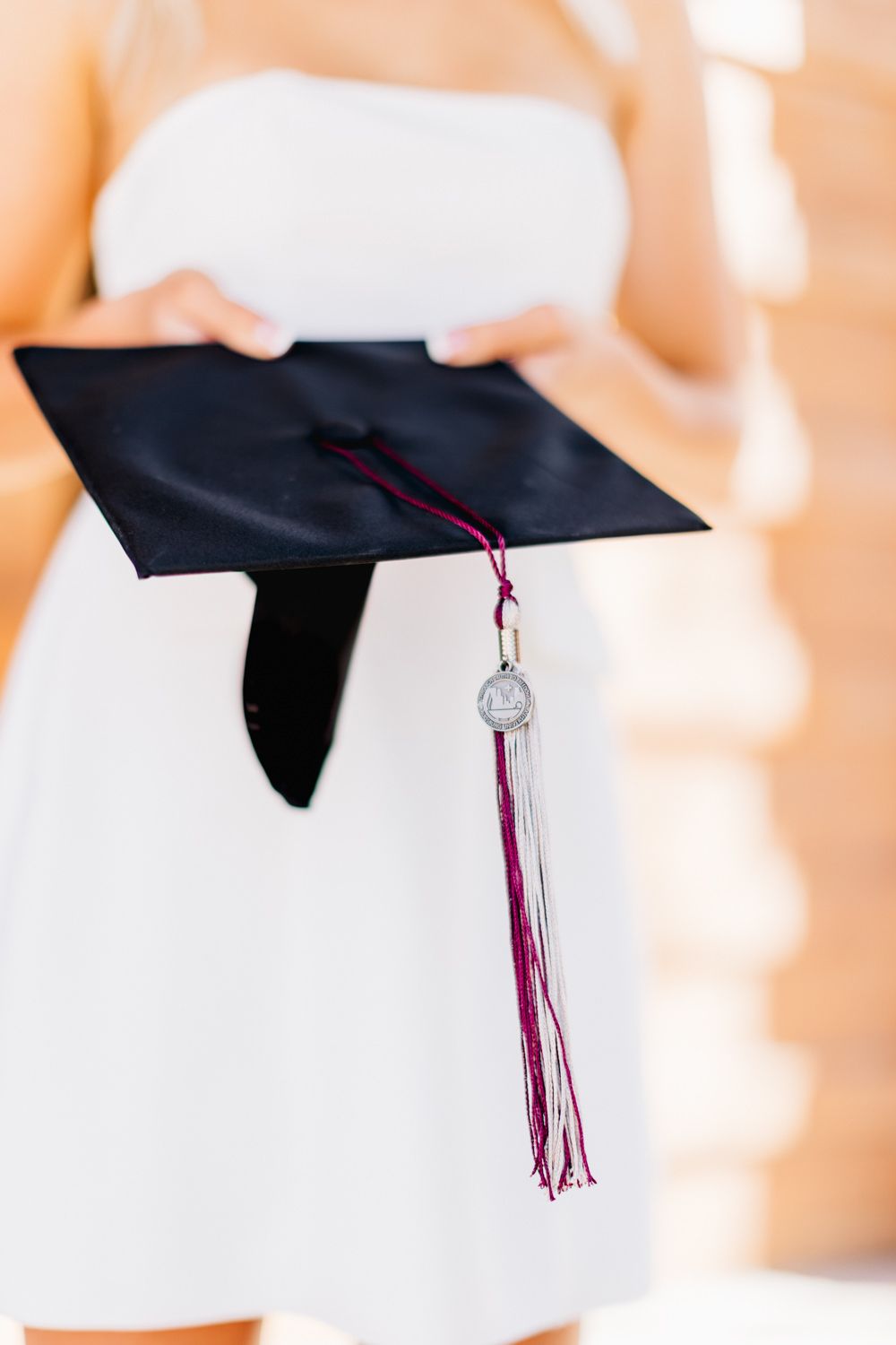 Close up of black graduation cap with burgundy tassel held against white dress.