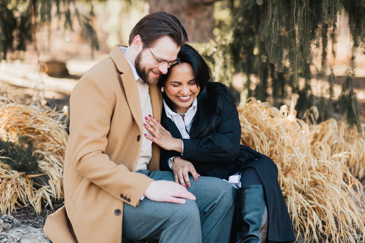 A couple shares a joyful moment together outdoors wearing winter coats in front of hanging moss.