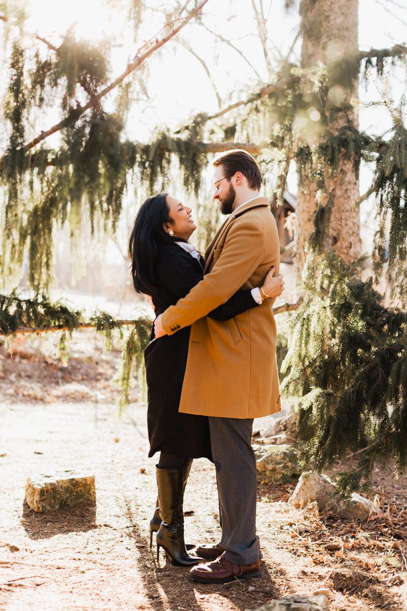 Romantic couple in contrasting coats embrace under Spanish moss during golden hour.