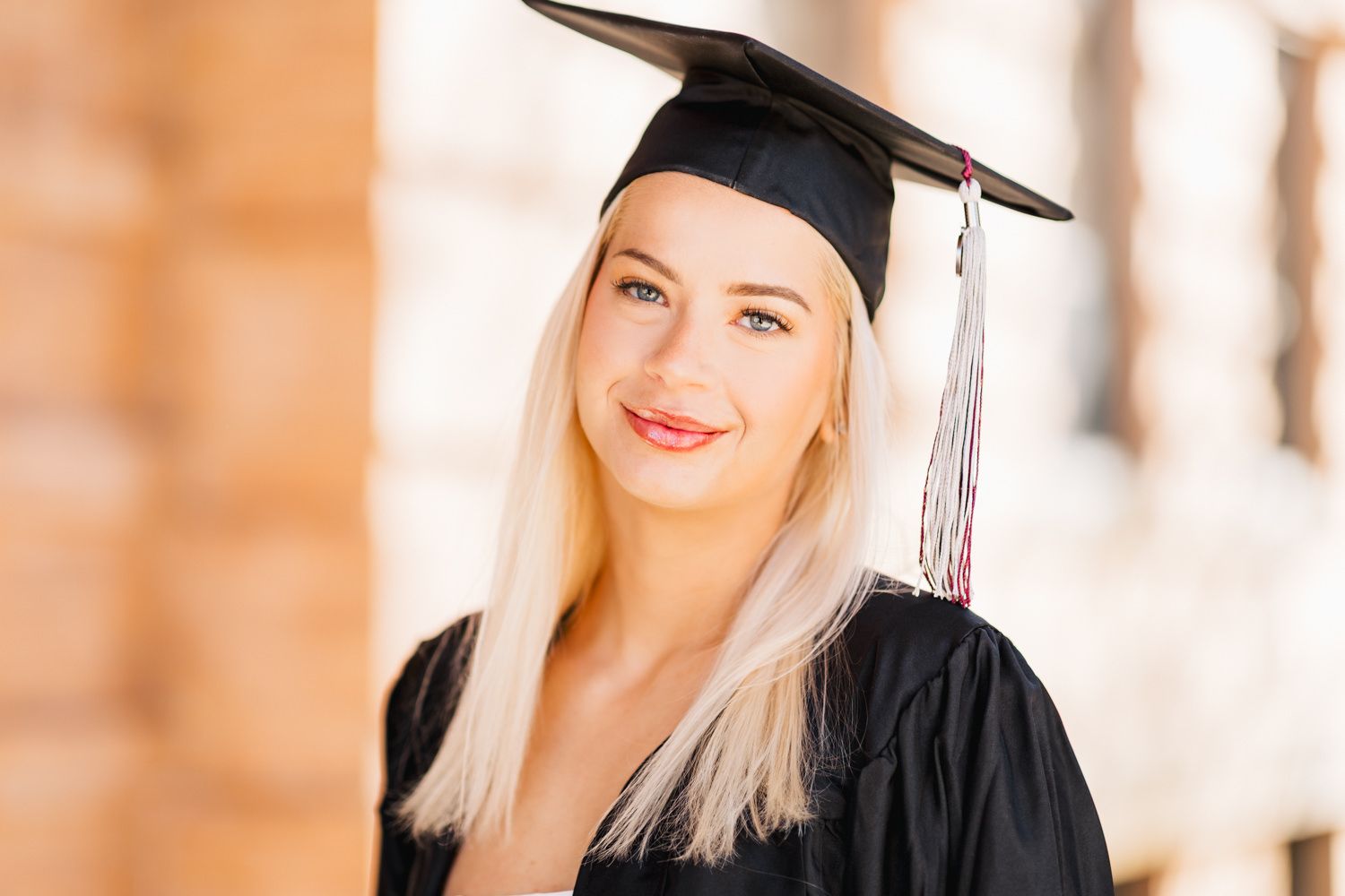 Graduation portrait with traditional black cap and gown against warm building tones.