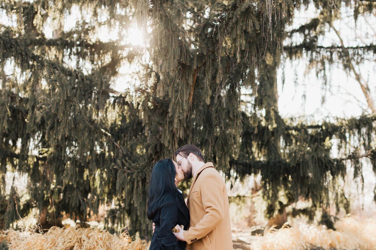 Two people embrace beneath moss-covered trees during a romantic outdoor moment.