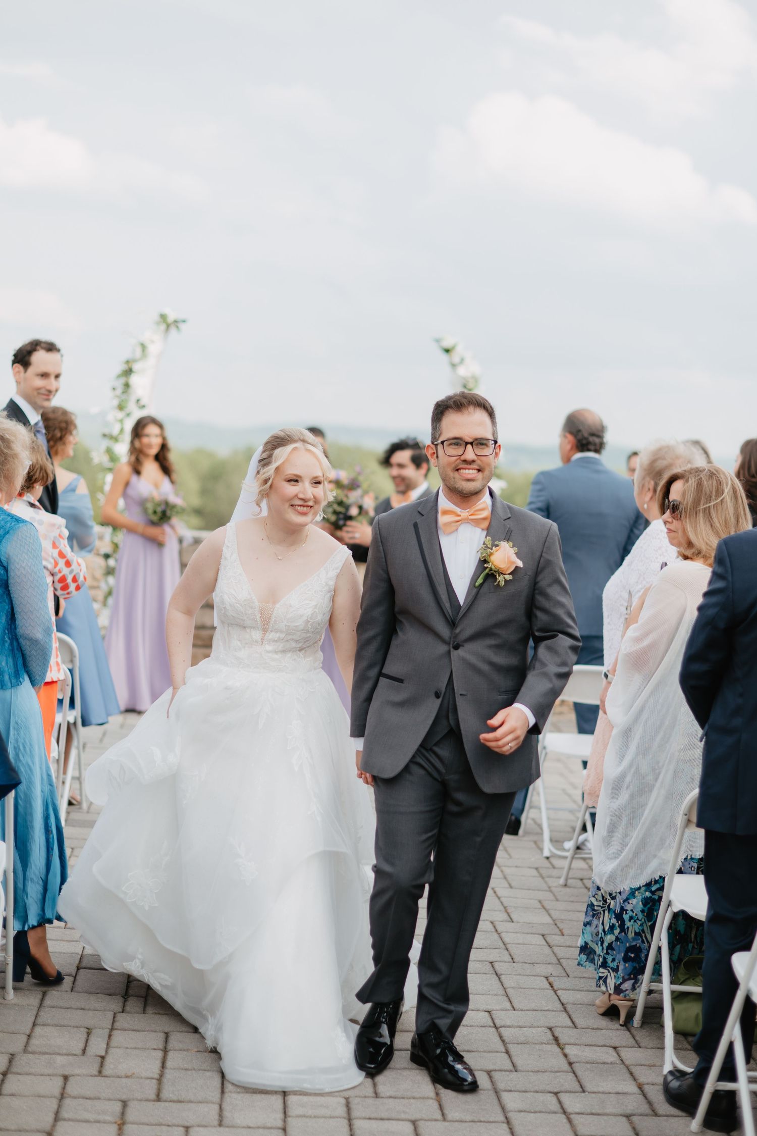 Straight couple leaving wedding ceremony hand in hand at an outdoor venue in Easton, PA with bright tones and muted greens.