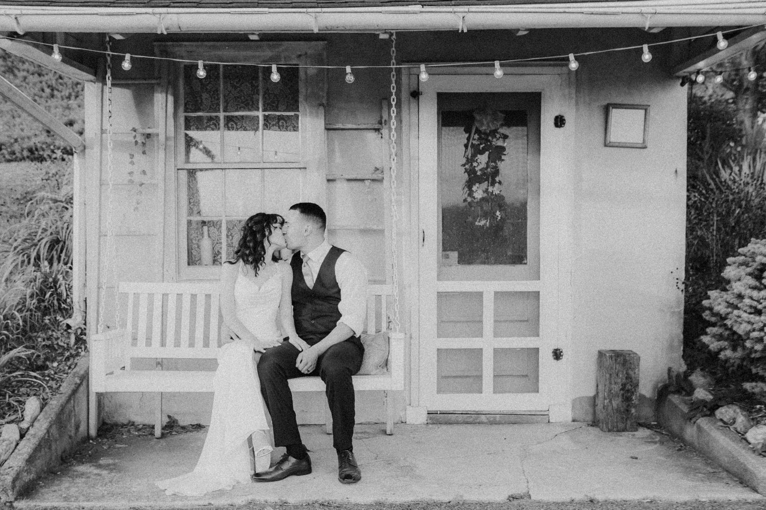 Elegant wedding portrait on a garden swing outside a quaint Pennsylvania cottage — the couple shares a quiet moment surrounded by greenery