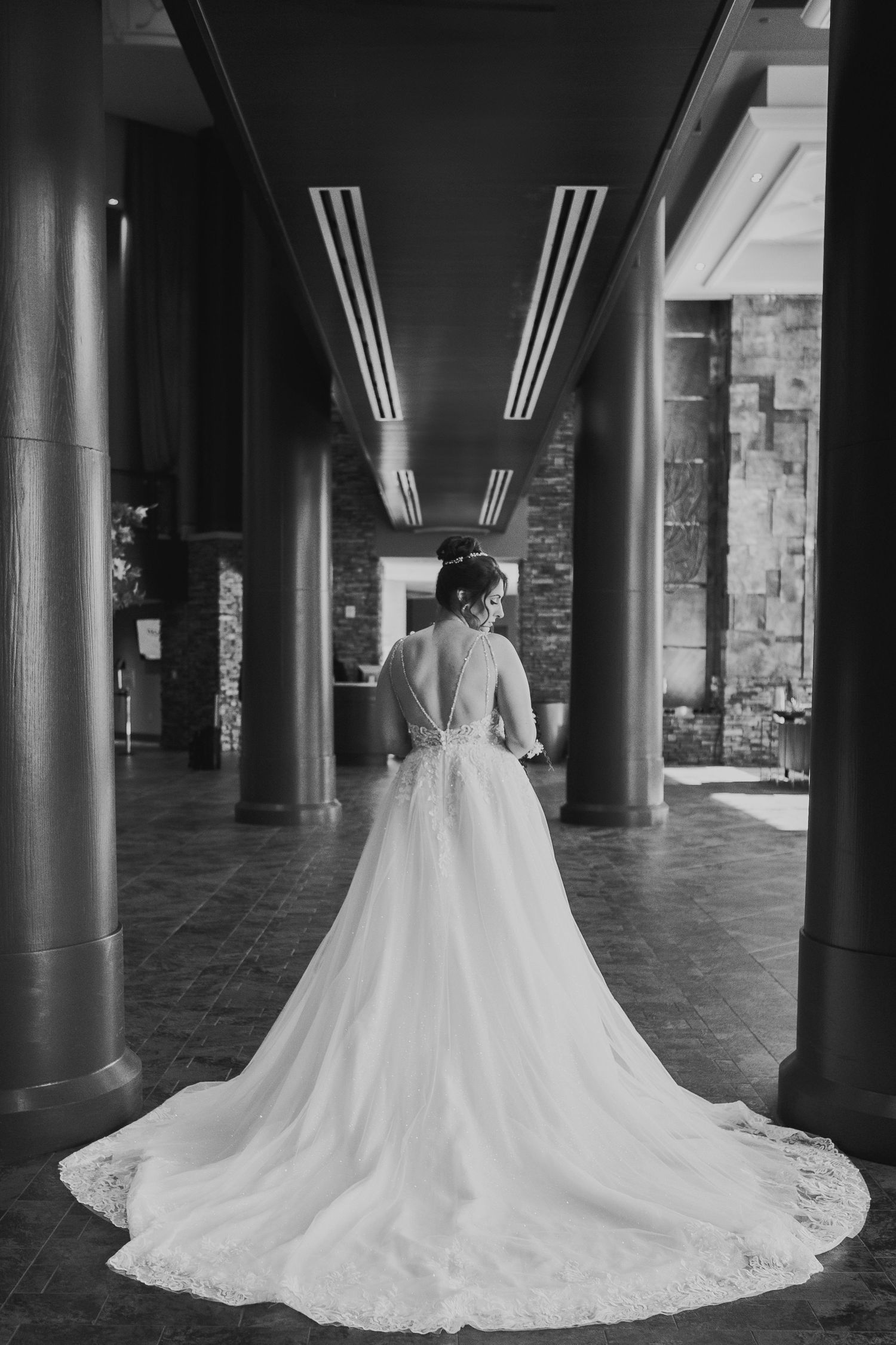 Back view of a bride in a flowing designer gown walking through a sunlit luxury hotel suite in Bethlehem, PA — a timeless, editorial-inspire