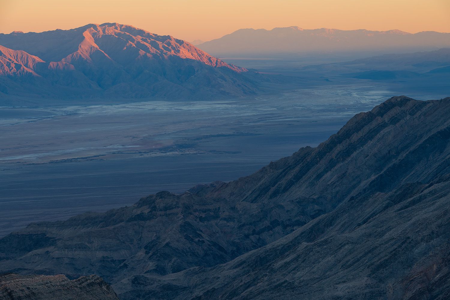 Desert mountains illuminated by warm sunset light with expansive plains stretching to the horizon.