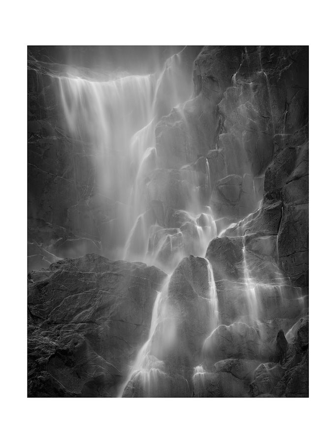 Majestic waterfall flowing over rocky cliffs captured in ethereal black and white.