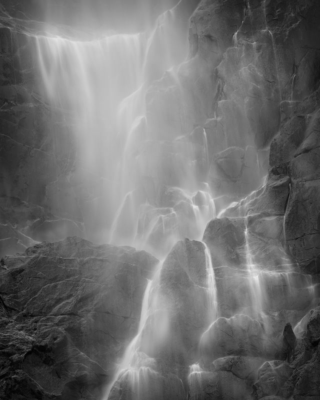 Dramatic black and white photograph of a cascading waterfall flowing over rocky cliffs.