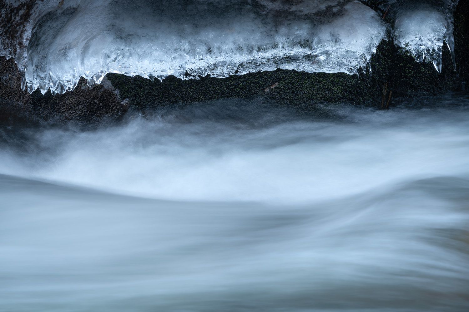 Long exposure of rushing winter stream with snow and ice along the banks.