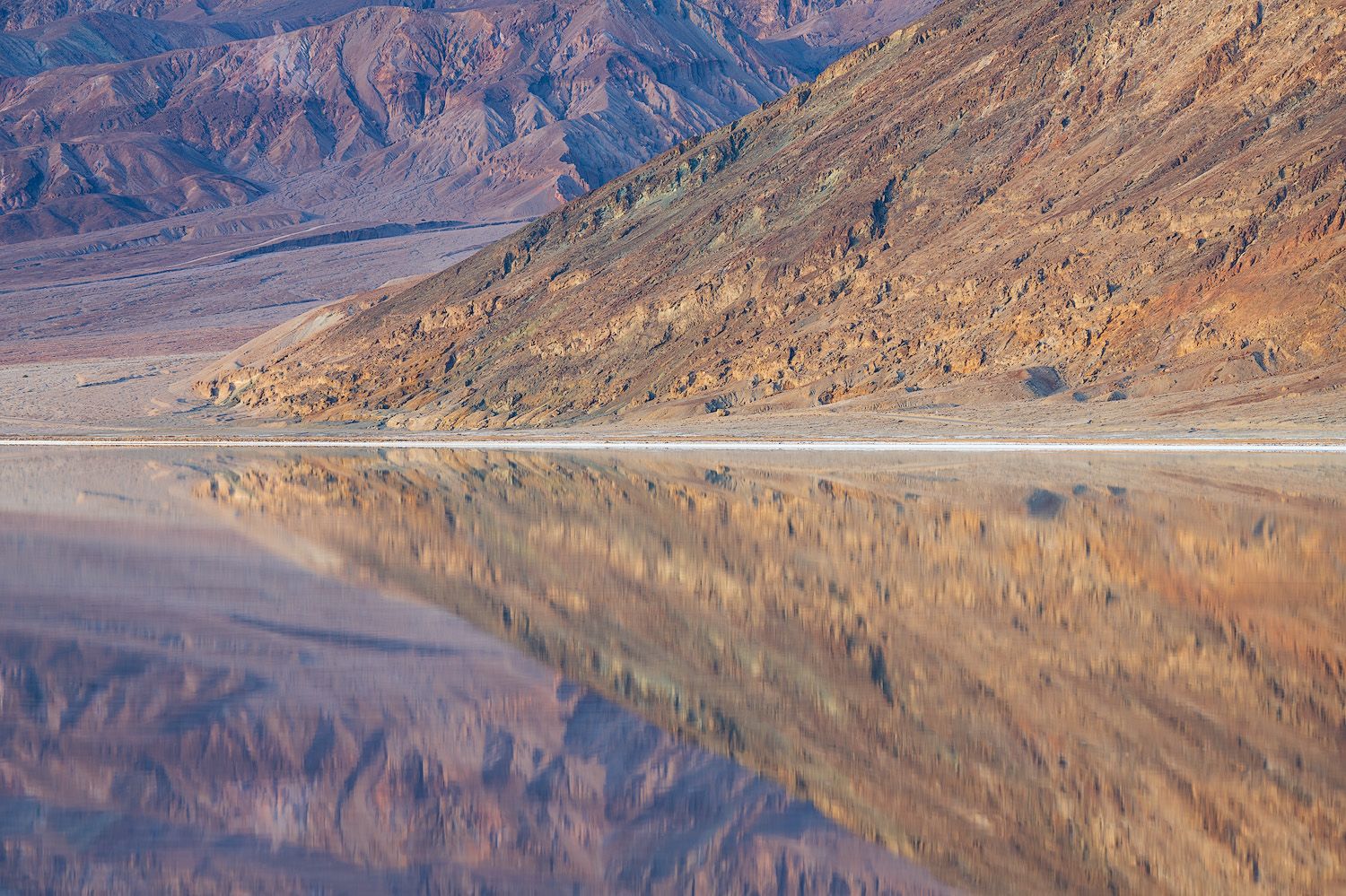 Mountain range reflecting in still lake waters during golden hour.