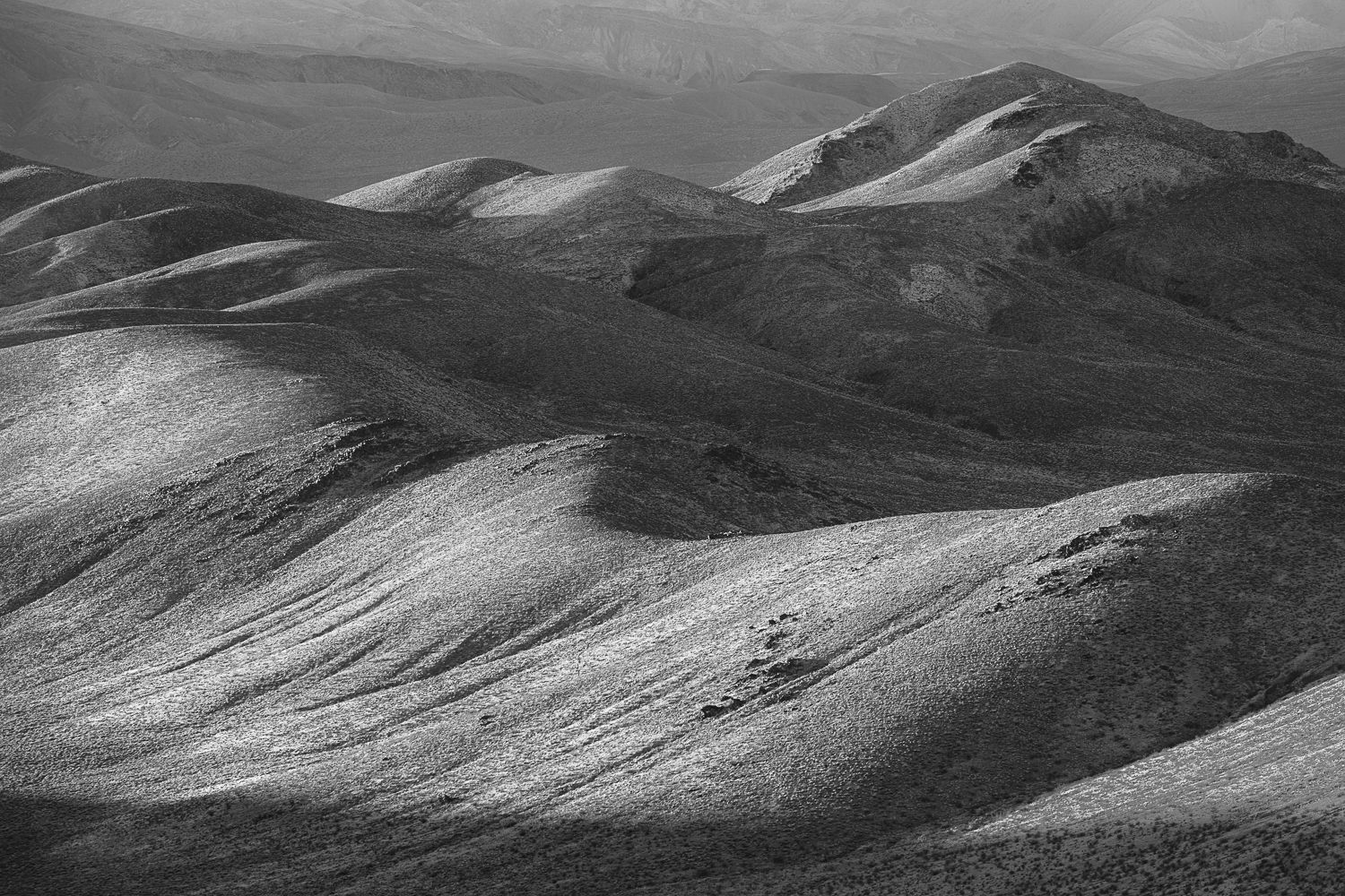 Rolling hills and mountains in black and white create a dramatic desert landscape with undulating shadows.