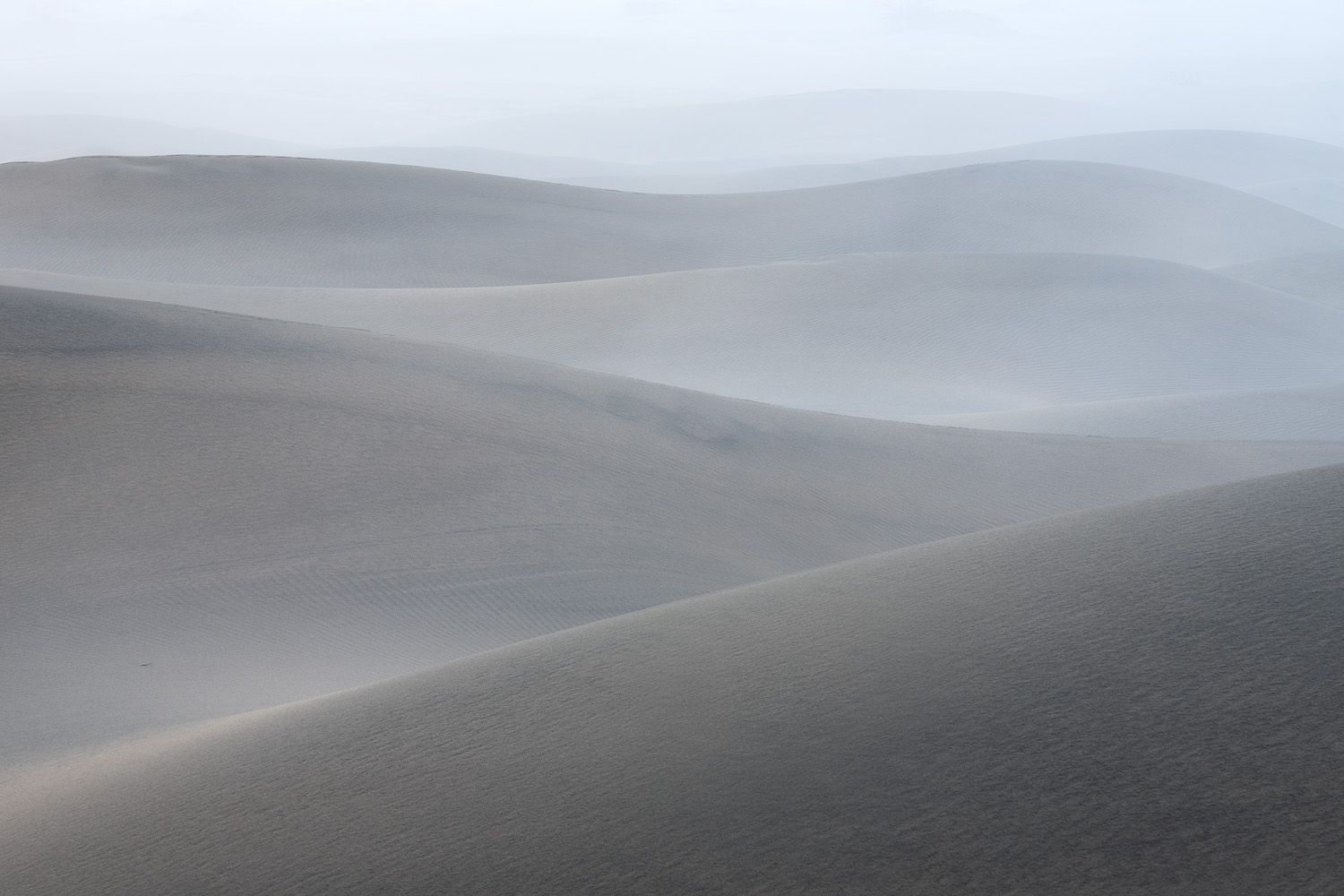 Foggy sand dunes create soft, ethereal curves in muted tones.