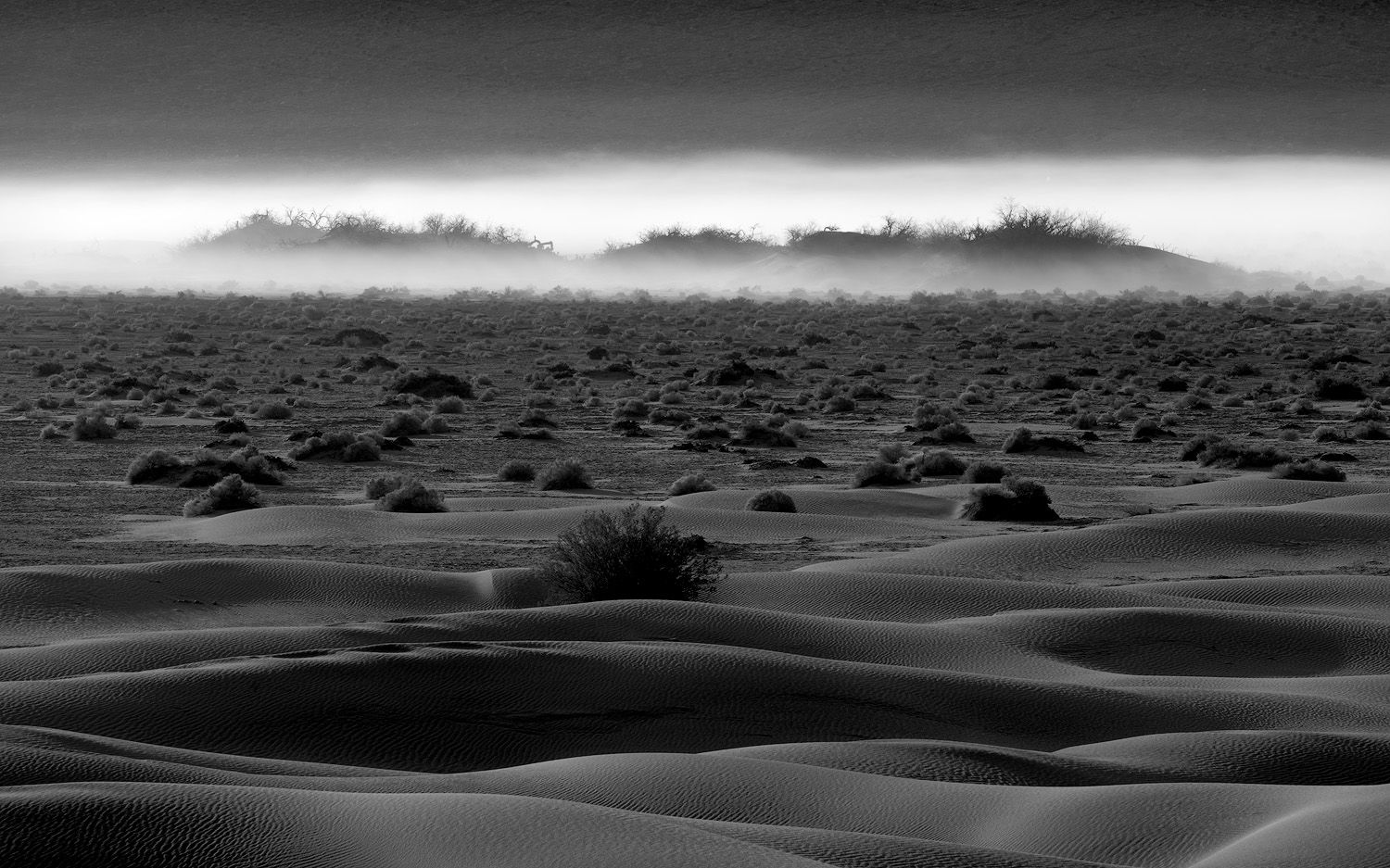 Desert sand dunes creating shadows and patterns in black and white photography.