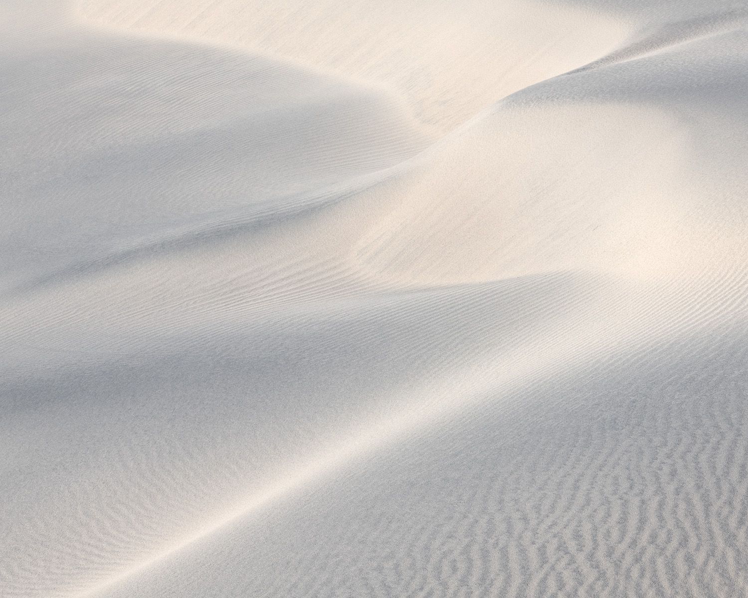 Smooth white sand dunes create flowing curves and ripples in soft natural light.