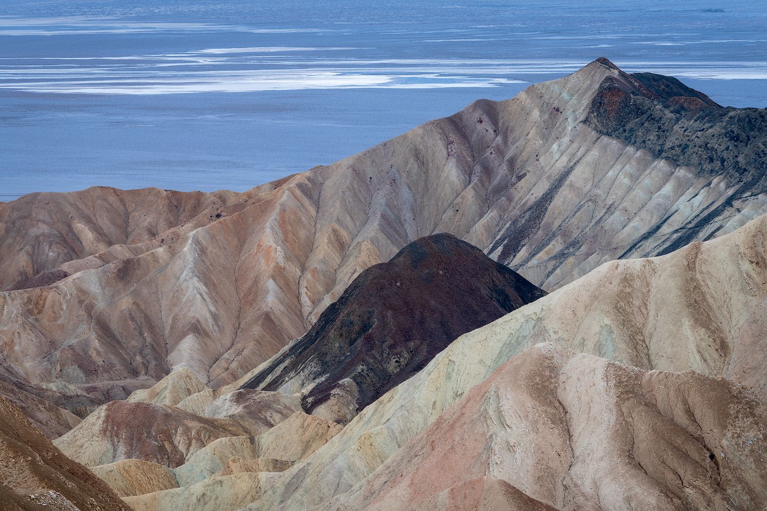 Colorful layered badlands with striped mineral deposits stretch toward a distant valley floor.