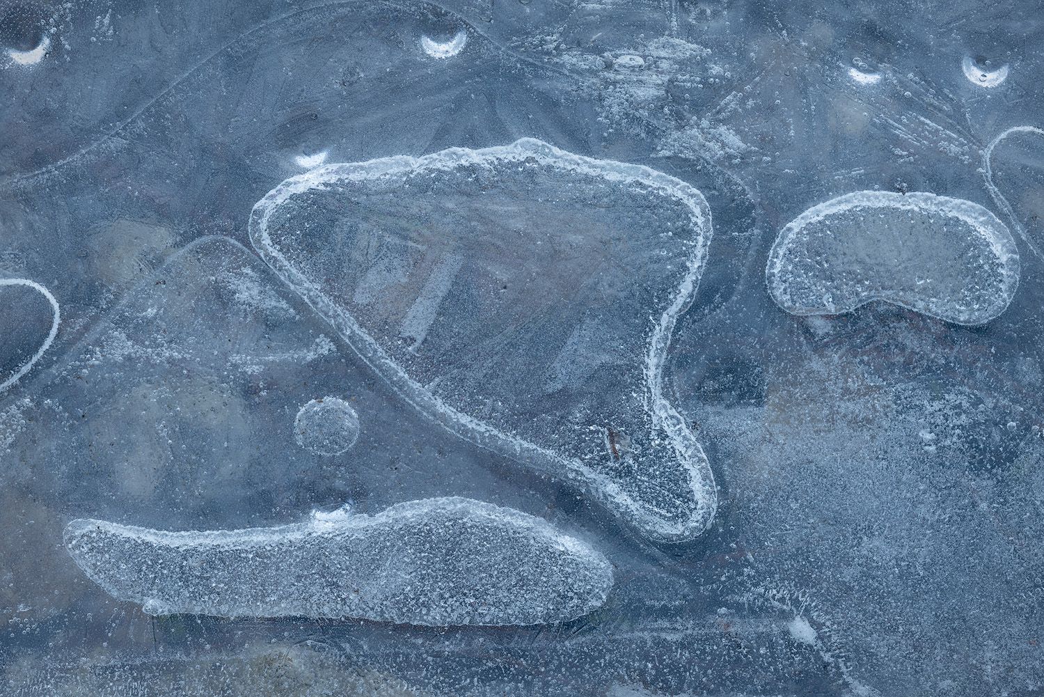 Abstract patterns formed by ice on a frozen river surface with circular formations.