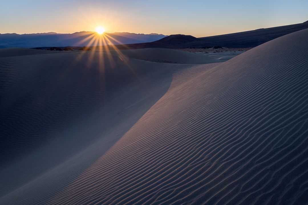 Stunning sunrise over sand dunes creates long shadows across desert landscape.