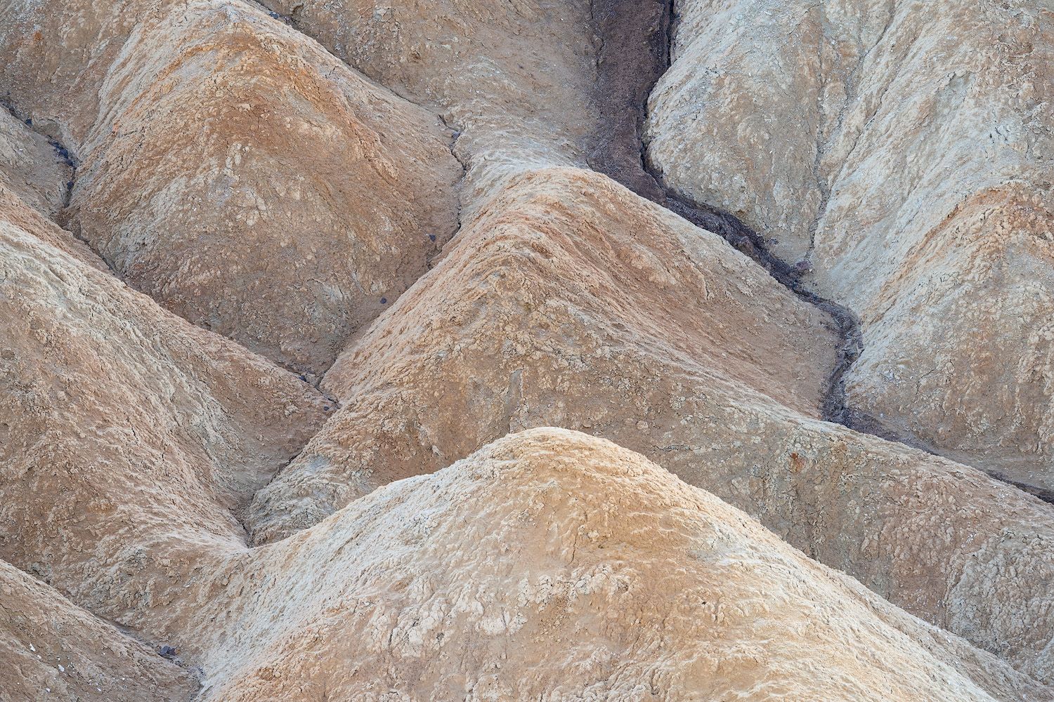 Textured beige rock formations create geometric patterns in eroded badlands.