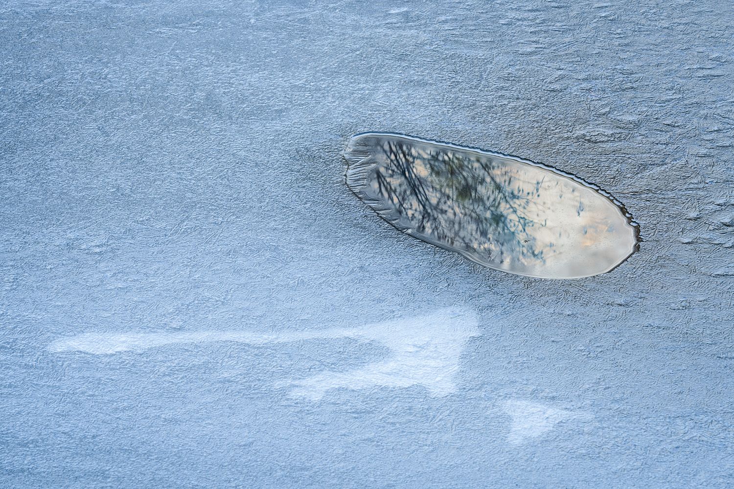 A hole in a layer of blue-tinted ice creates a minimalist winter scene.