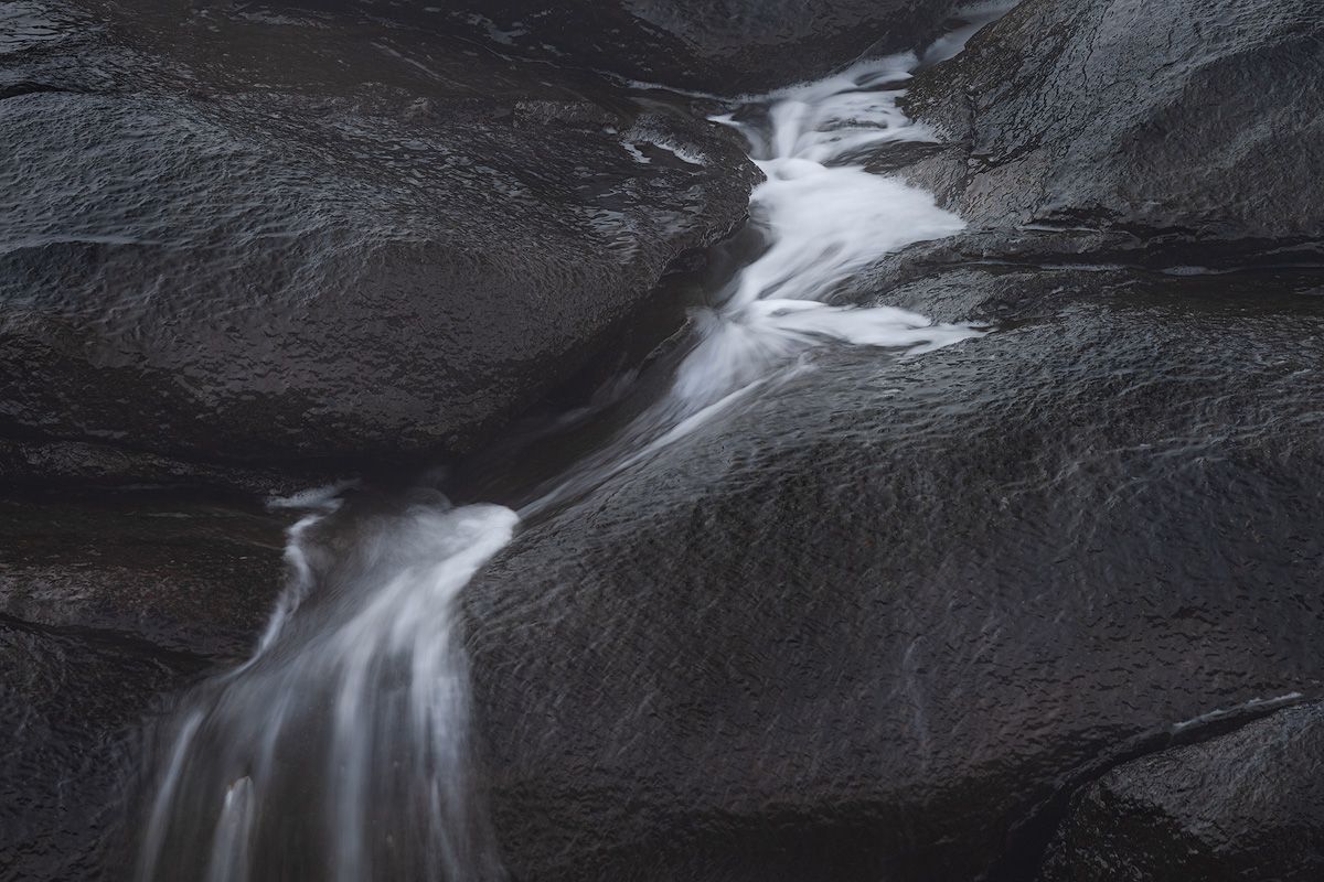 Long exposure waterfall creates silky white streams over dark rocky surface.