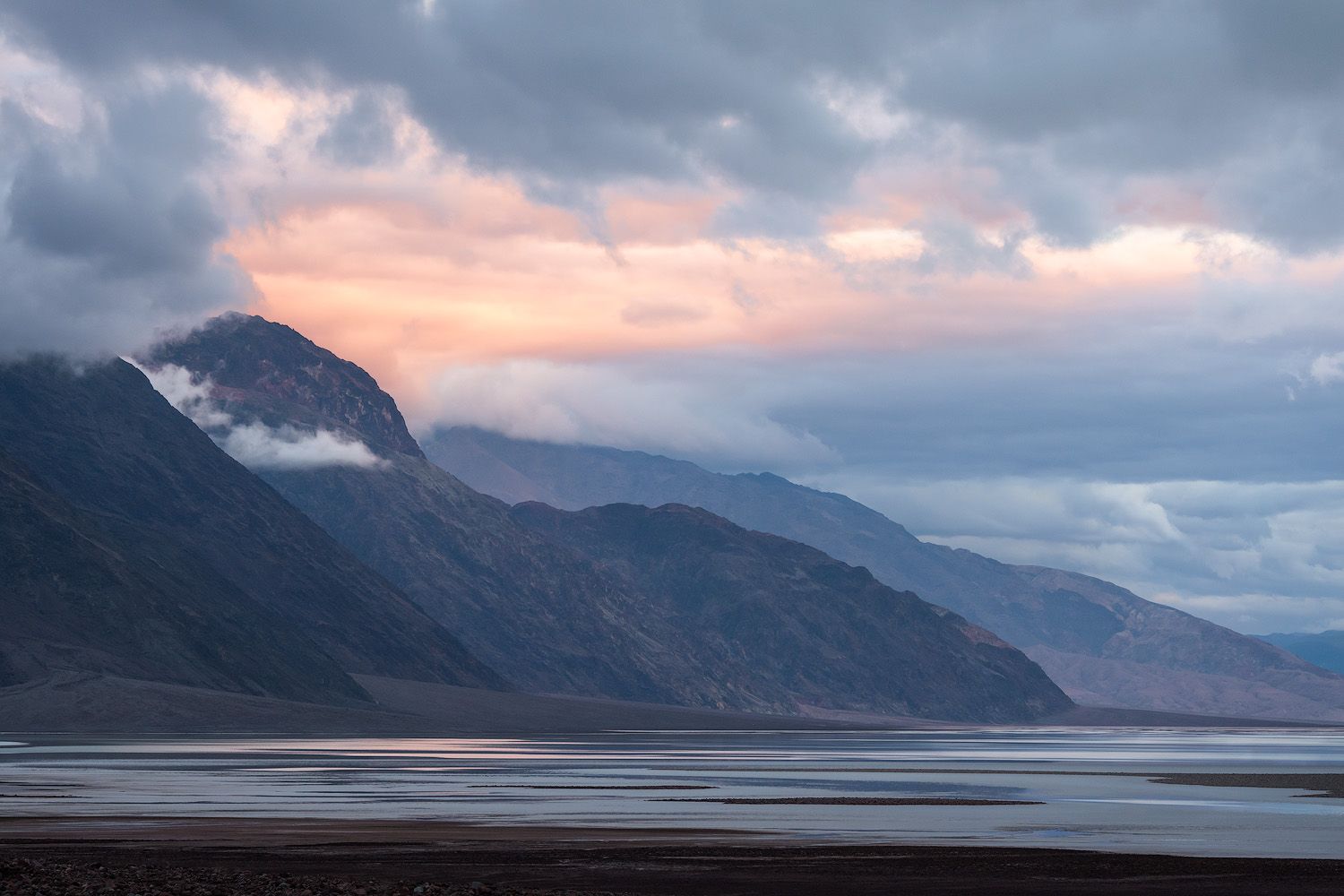 Dramatic sunset over mountains with fog rolling across a vast salt flat basin in Death Valley.