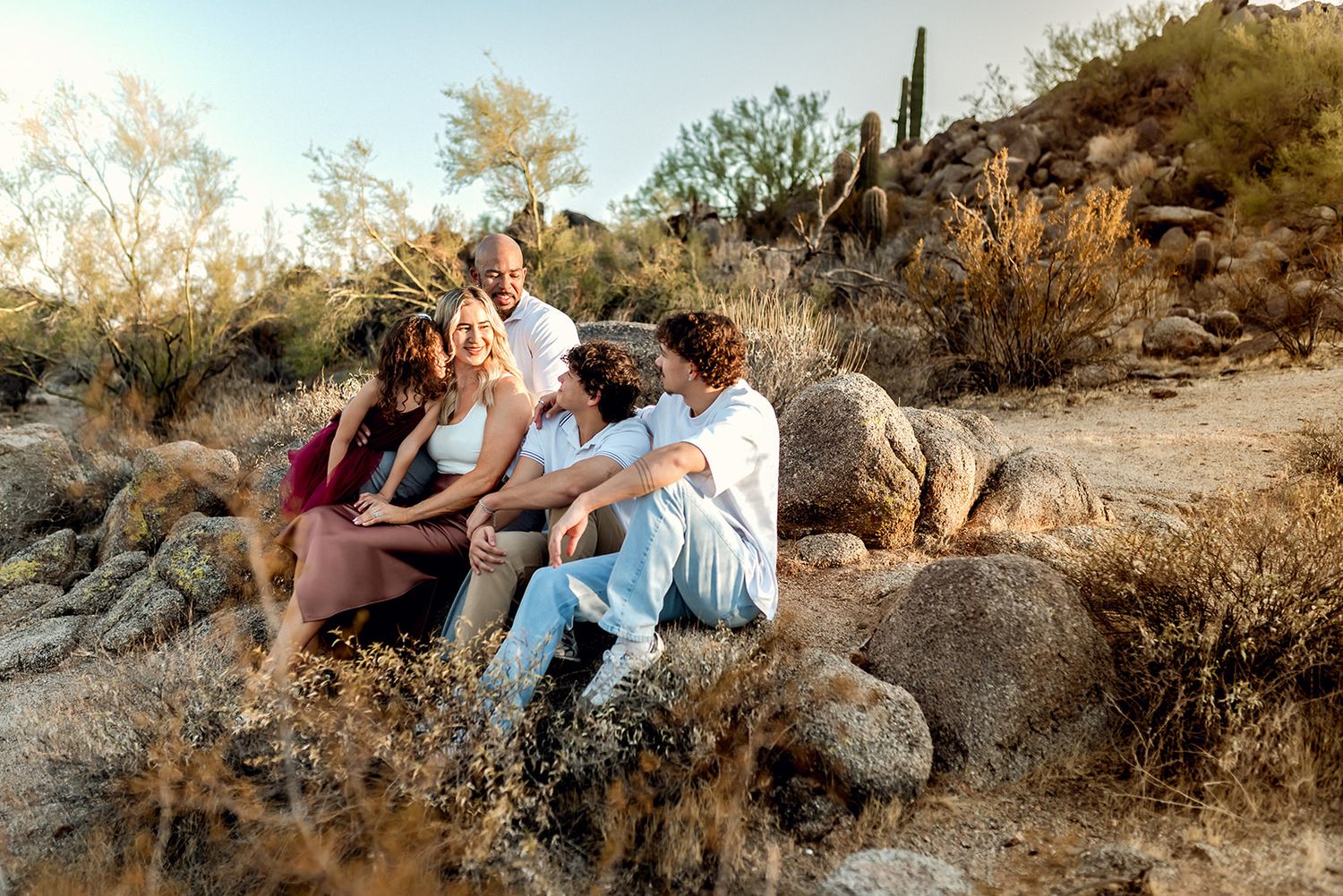 A group sits together on desert rocks at golden hour among saguaro cacti and desert terrain in the Arizona landscape.