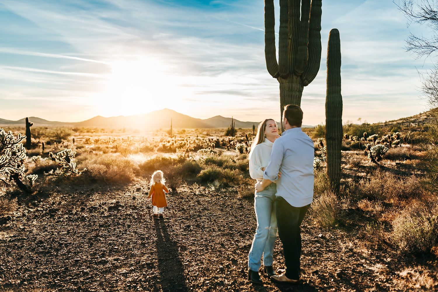 A beautiful desert sunset illuminates a family standing among tall saguaro cacti in the Arizona desert landscape.