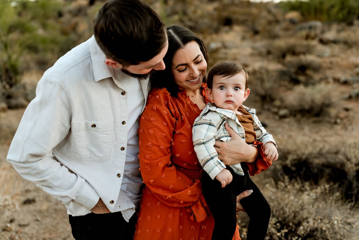 Desert lifestyle photoshoot shows people in white and rust colored outfits standing close together among desert brush.