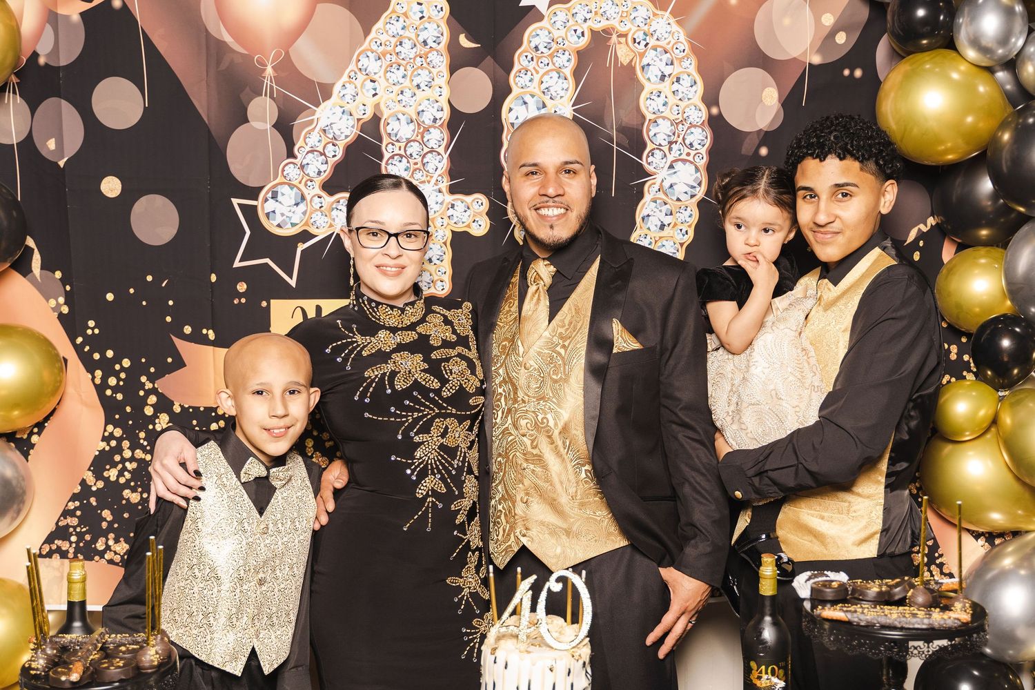 Family posing at 40th birthday party with gold and black decor and champagne-themed backdrop – NYC event photo.
