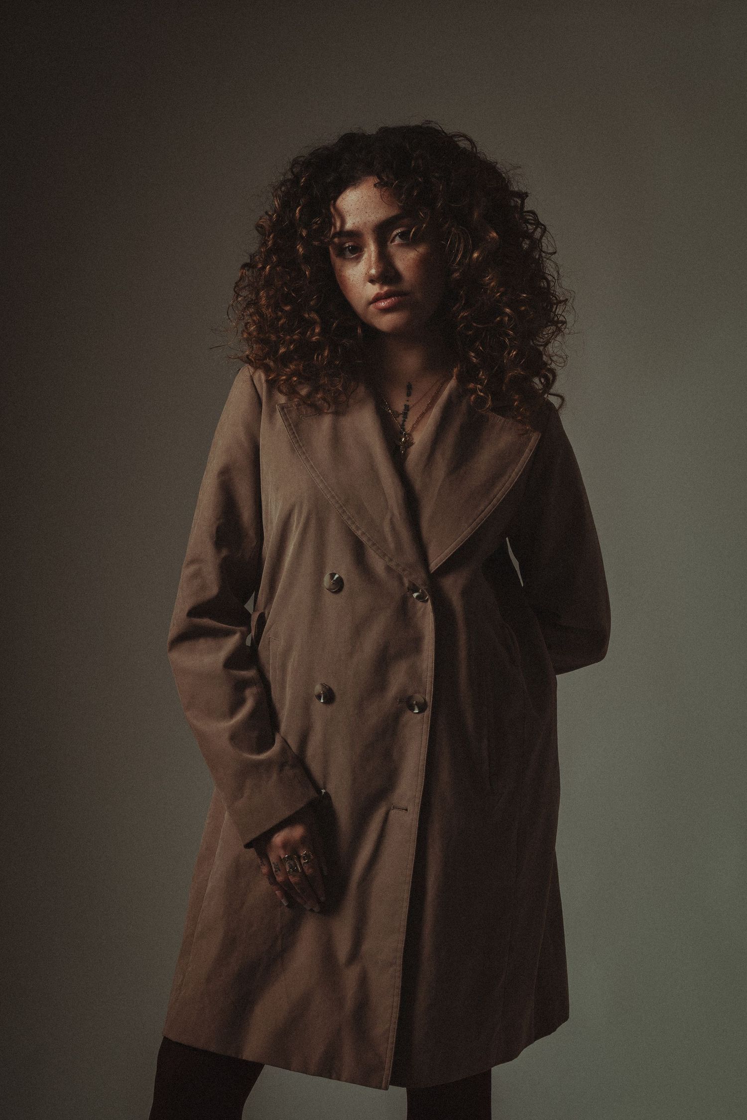 Moody portrait of curly-haired woman in trench coat, shot in dramatic low light – NYC editorial session.