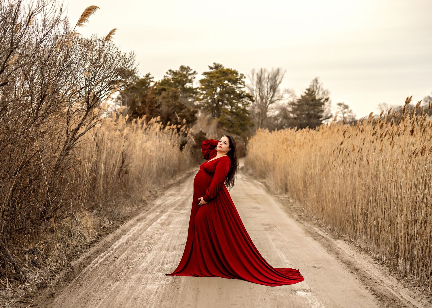A flowing red dress stands out against golden reeds and a dirt path during sunset in a natural setting.
