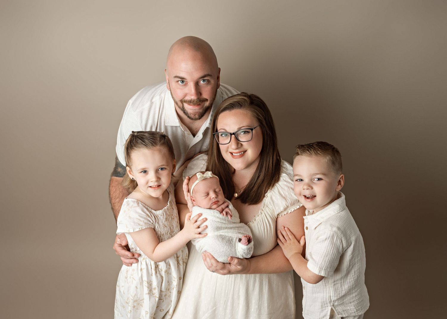 A family of five wearing white outfits poses together for a formal studio portrait against a neutral backdrop.