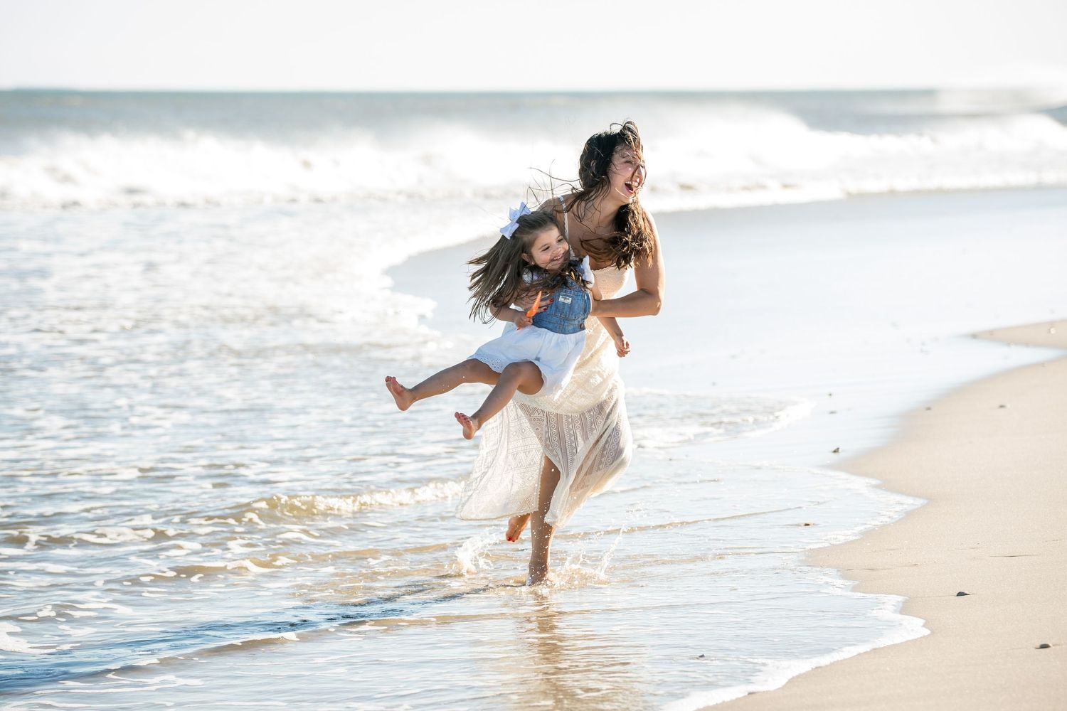 People playing and laughing together on a sunny beach with ocean waves in the background.