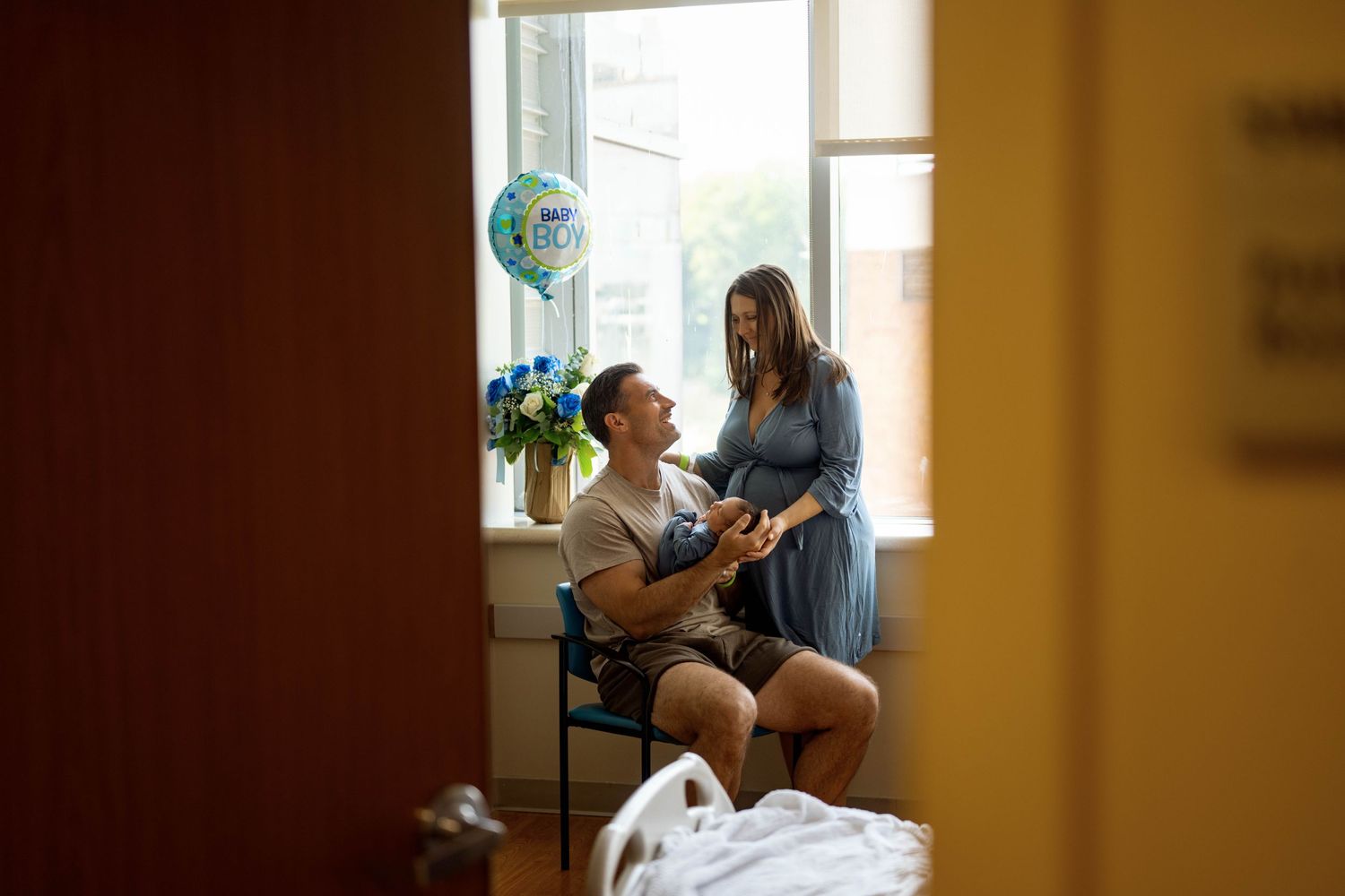 Two people interact in a warmly lit room near a window with houseplants visible in the background.