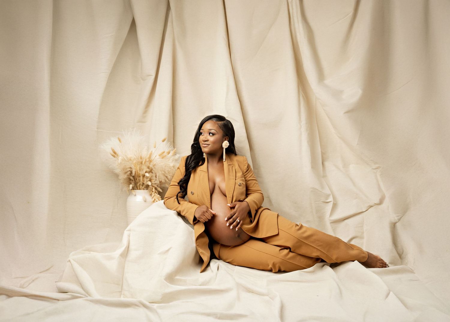 Stylish model wearing beige monochromatic outfit poses elegantly on cream backdrop with dried pampas grass arrangement.
