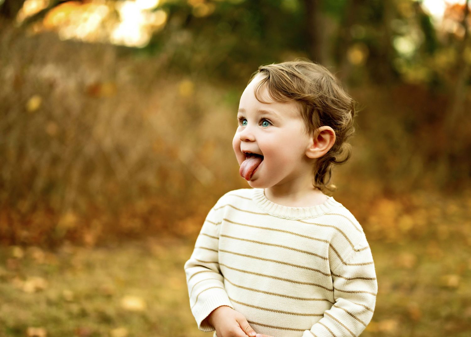Small child wearing striped sweater laughs joyfully outdoors during golden hour in autumn setting.