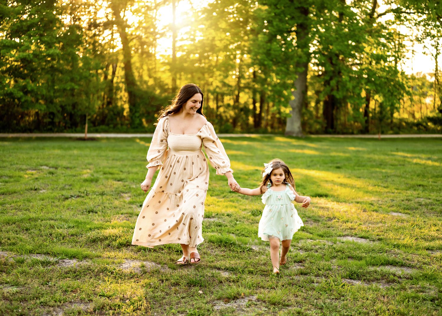 A family in matching floral dresses walks and plays together in a sunlit grassy field during golden hour.