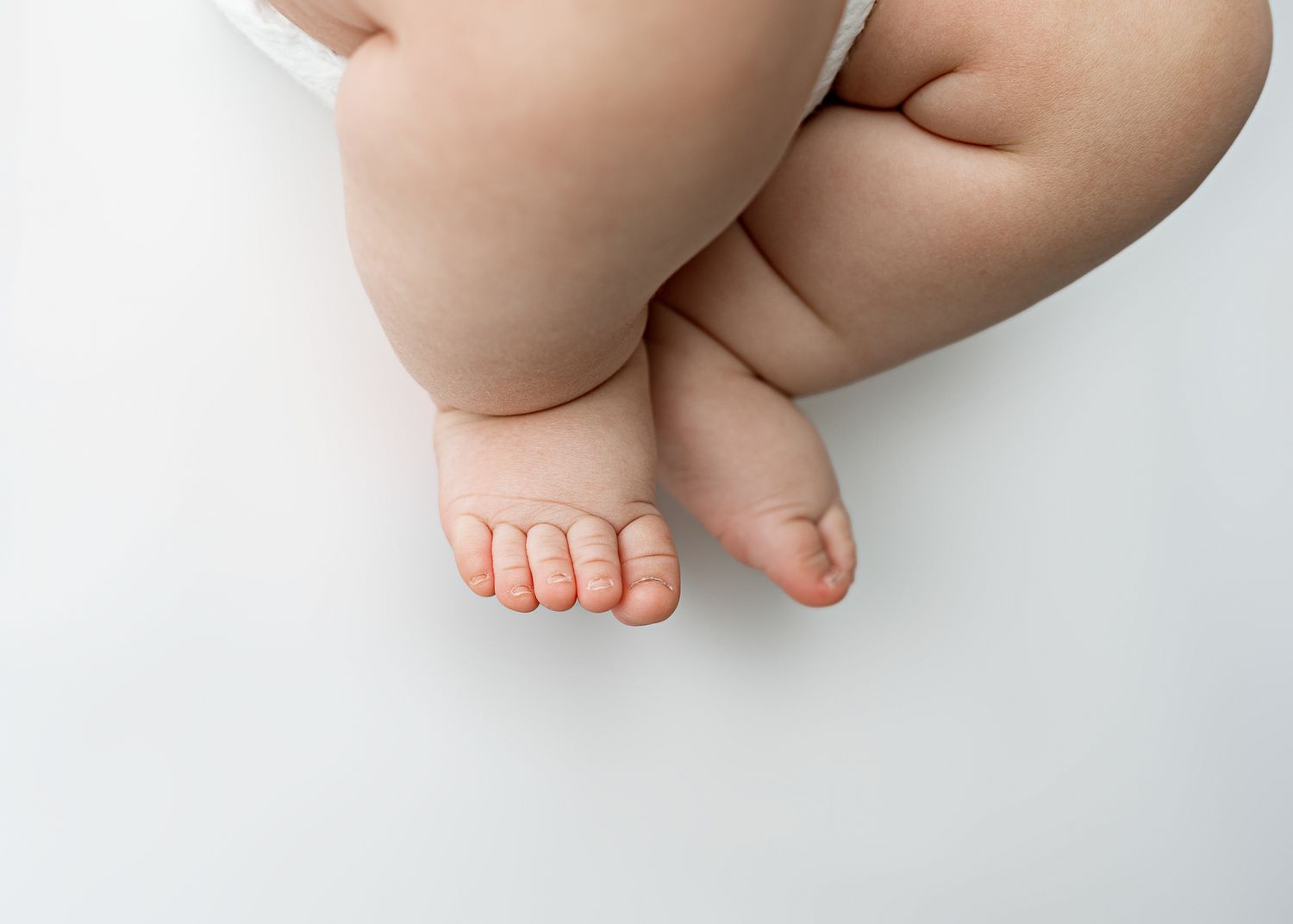 Tiny baby feet and chubby legs resting on a white background showing soft delicate skin.