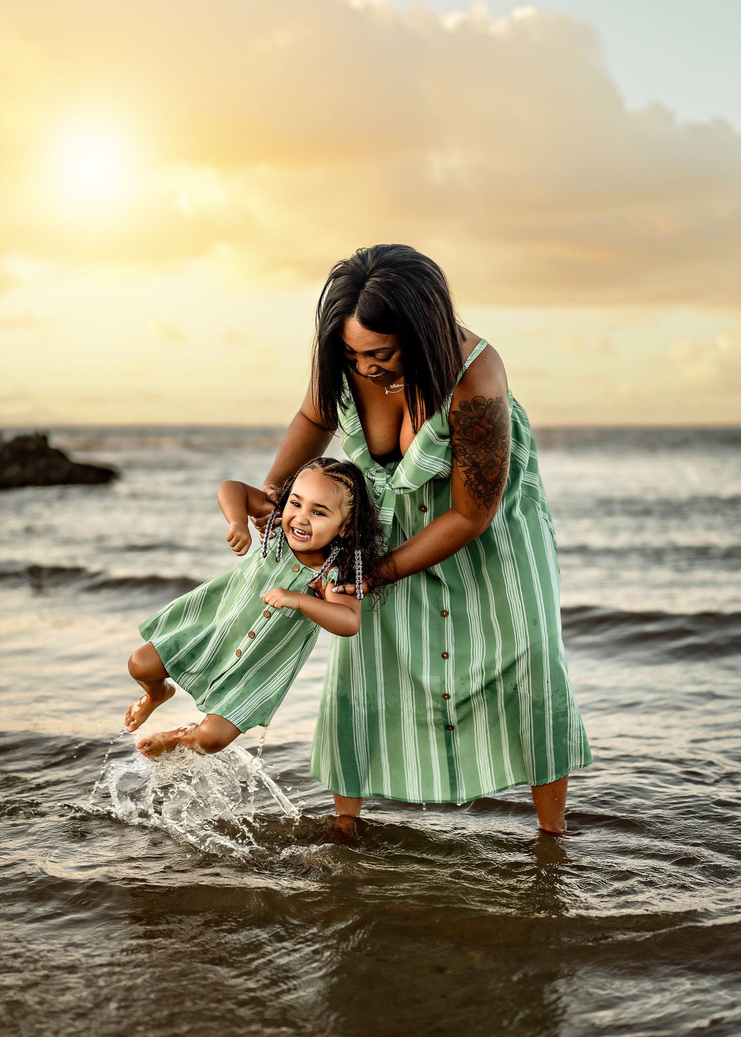 A joyful moment at sunset as two figures in matching mint green dresses splash and play in the ocean waves.