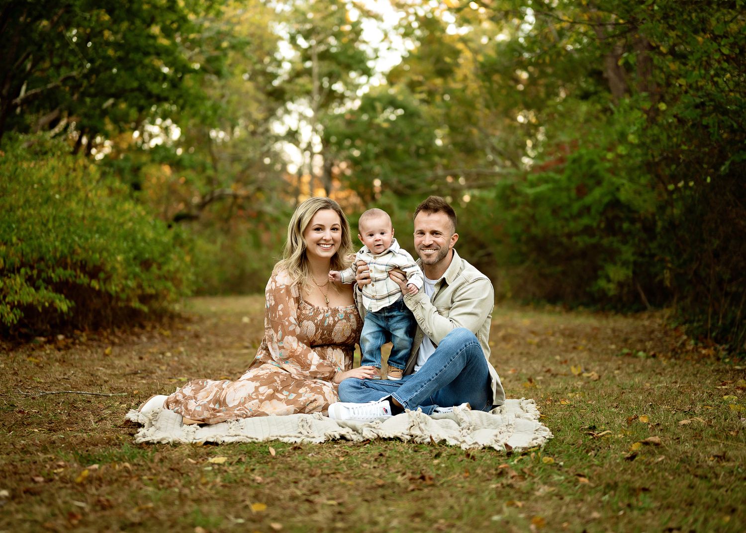 Three people sitting on a white blanket outdoors having a picnic in a wooded area during autumn.