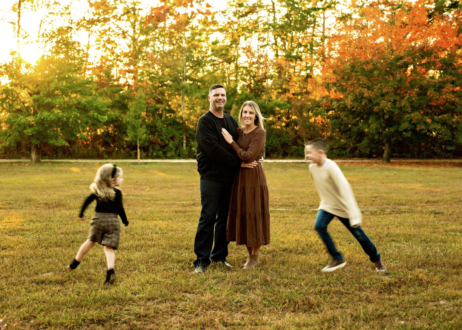Family enjoying a playful moment together in an autumn field at sunset with fall foliage in the background.