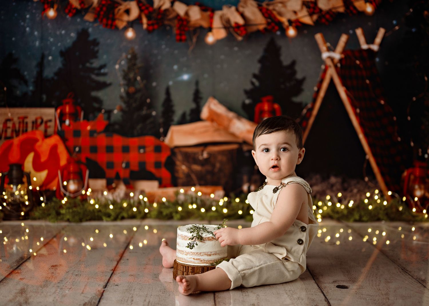 A toddler sits on wooden floor with cozy holiday decorations and string lights creating a warm, festive atmosphere.