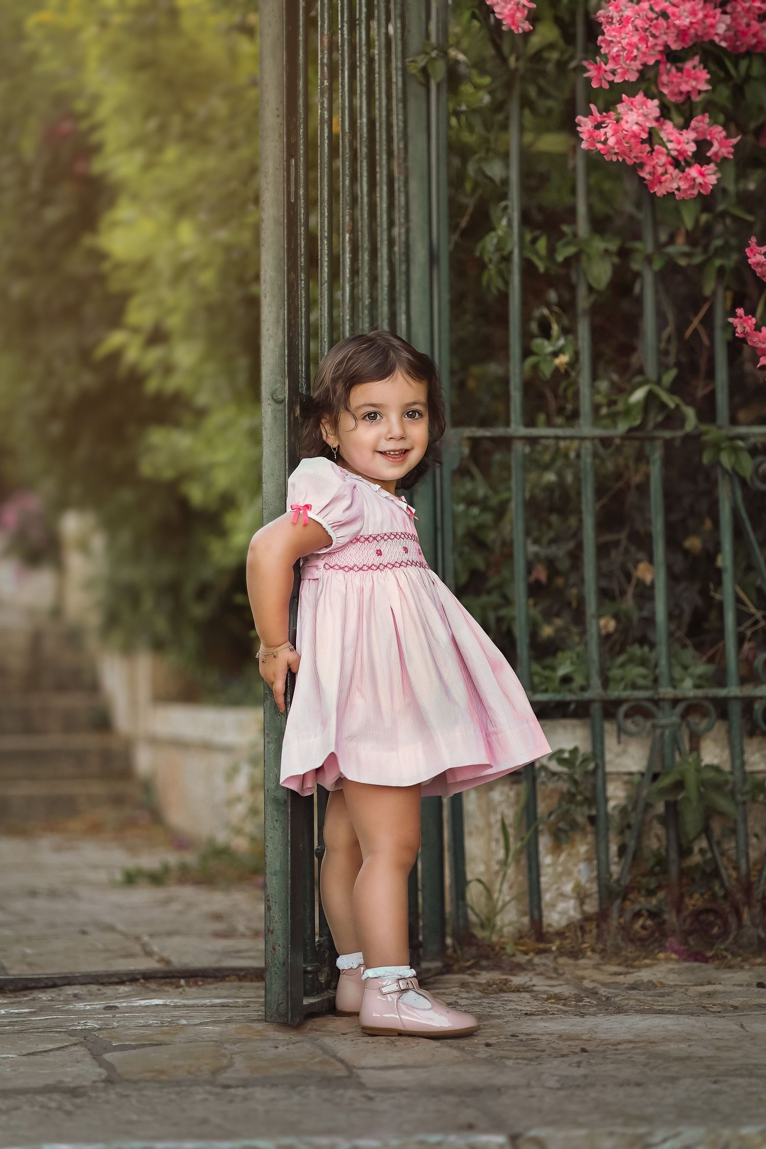 Pink flowering branches frame a charming garden scene with wrought iron gates in spring.